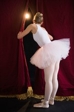 Teenage (16-17) ballerina on stage looking through curtain