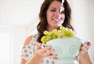 Portrait of young woman washing grapes in colander