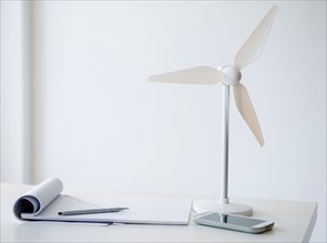 Studio Shot of small wind turbine, mobile phone and note pad on desk
