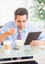 View of mature man eating cereal and using digital tablet