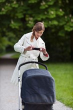 Mother with pram in park taking picture with cell phone