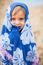 Baby girl (2-3) wrapped in towel on beach