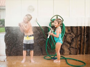 Children (2-3, 6-7) refreshing with garden hose