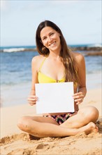 Portrait of young woman with blank paper sitting on beach