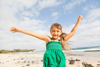 Portrait of girl (6-7) standing on beach with arms raised