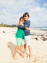 Portrait of girl (6-7) and boy (10-11) embracing on beach