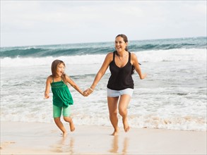 Girl (6-7) running on beach with mother