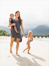 Mother walking with daughters (6-11 months, 2-3) on beach