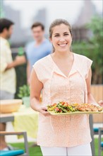 Woman carrying tray with food in garden.