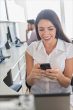 Woman text messaging in office, man in background.