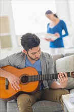 Man playing guitar, woman in background.