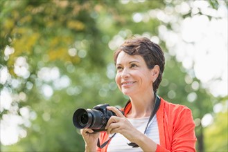 Mature woman holding camera in park.