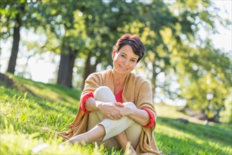 Mature woman sitting on grass in park.