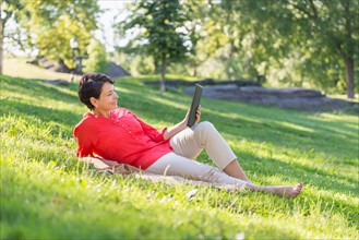 Mature woman lying on grass and using digital tablet.