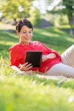 Mature woman lying on grass and using digital tablet.