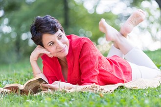 Mature woman lying on grass and reading book.