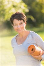 Mature woman holding yoga mat outdoors.