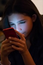 Girl (12-13) texting on mobile phone at night.