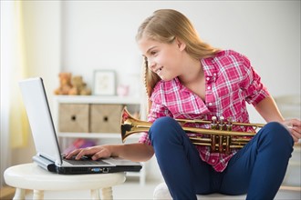 Girl (8-9) with trumpet using laptop