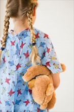 Rear view of blond girl (8-9) in hospital holding teddy bear