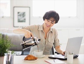 Portrait of woman pouring coffee in front of laptop