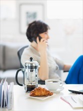 Woman talking on phone, coffee and croissant in foreground
