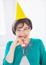 Portrait of woman wearing party hat and holding party horn blower
