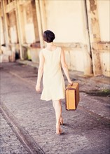 Rear view of woman in dress carrying suitcase at train station