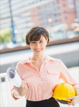 Portrait of smiling woman holding blueprints and hard hat