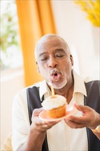 Portrait of man holding cupcake and blowing out candle
