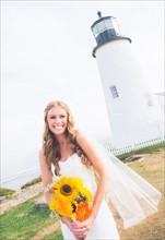 Portrait of smiling bride holding sunflower bouquet, lighthouse in background
