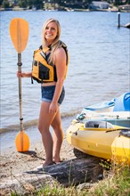 Portrait of young woman holding oar on lake shore