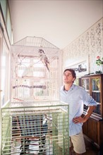 Portrait of young man standing by bird cage and looking at parrot