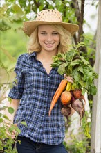 Portrait of young woman holding fresh vegetables in garden
