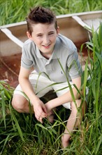 Boy (12-13) crouching on grass near boat