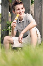 Boy (12-13) sitting in grass and eating ice cream