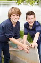 Two boys (12-13) posing with boat on grass near lake