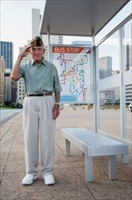 Senior man standing and saluting at bus stop