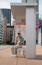 Senior man sitting at bus stop and using mobile phone