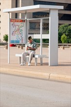 Senior man sitting at bus stop and text messaging