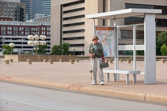 Senior man standing at bus stop with fishing rod