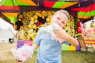 Boy (4-5) eating cotton candy in amusement park