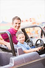 Father with son (4-5) driving toy car in amusement park