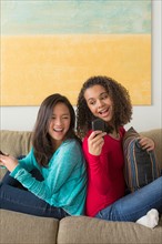 Two friends (12-13,16-17) sitting on sofa and playing with smartphone