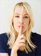 Studio portrait of blonde woman with finger on lips