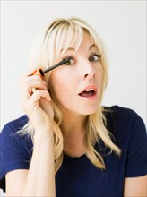 Studio portrait of blonde woman applying mascara