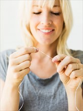 Studio portrait of blonde woman cleaning teeth with dental floss