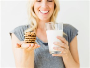 Studio portrait of blonde woman holding glass of milk and cookies