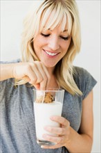 Studio portrait of blonde woman dipping cookie in milk