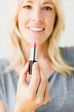 Studio portrait of blonde woman holding pink lipstick